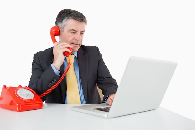 Ernstige mens die terwijl het schrijven op laptop telefoneert