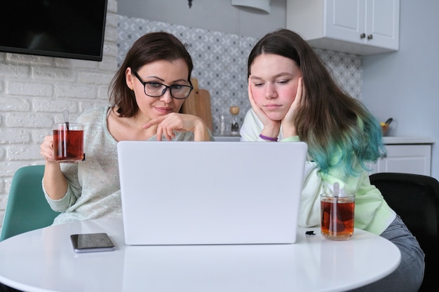 Ernstige moeder en tienerdochter om thuis te zitten aan tafel, laptop computer kijken. Onaangename informatie, ongelukkige trieste video