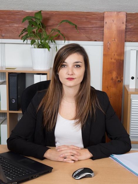 Ernstige, mooie zakenvrouw die een notitieboekje presenteert dat aan haar bureau zit en naar de camera kijkt