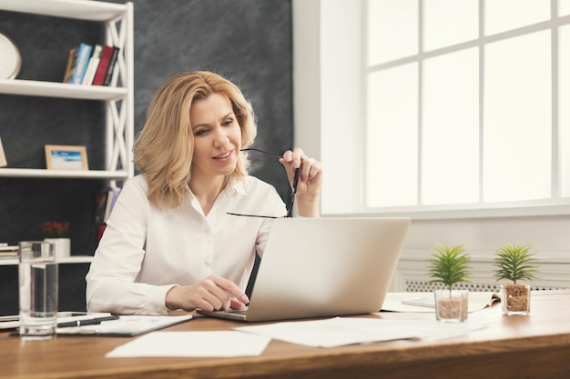 Ernstige onderneemster die aan laptop op kantoor werkt. Zakenvrouw met een bril die iets op de computer typt terwijl ze op haar werkplek zit, kopieer ruimte