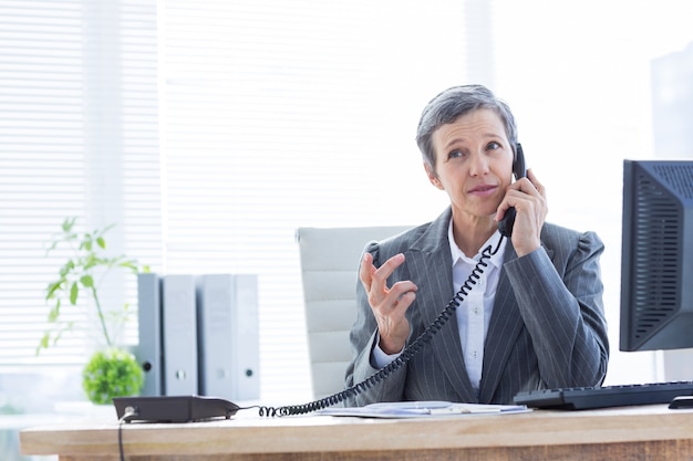 Ernstige onderneemster die en computer met behulp van telefoneert