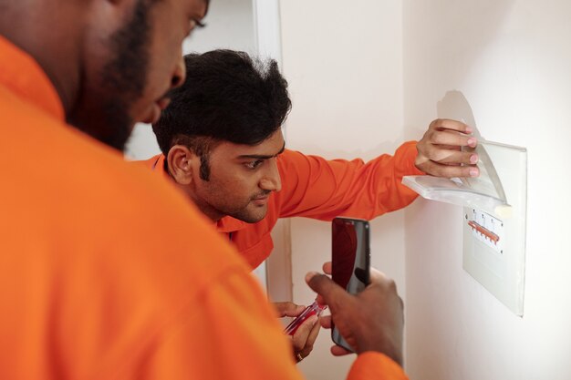 Ernstige professionele elektriciens in oranje uniform installeren watt-uurmeter in appartement op klant