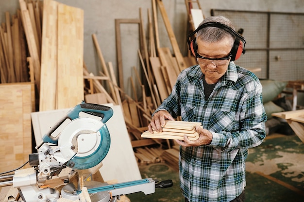 Ernstige schrijnwerker in profective oorkappen en bril sneed houten plank in vier stukken