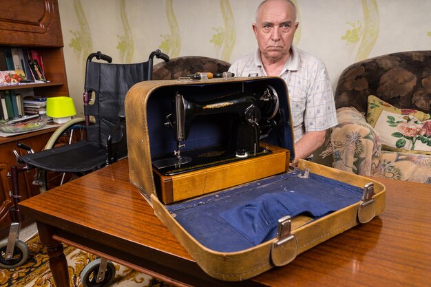 Ernstige Senior kleermaker toont zijn handmatige naaimachine in een draagtas bovenop de tafel in de woonkamer.