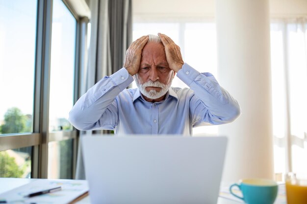 Ernstige senior man die op laptop werkt, leest zakelijk nieuws, kreeg slecht nieuws, leert bankafschriftinformatie Postcorrespondentieconcept