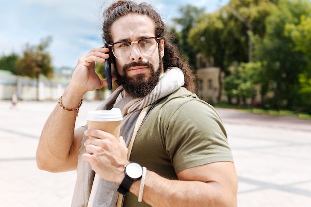 Ernstige slimme man die een telefoongesprek voert terwijl hij een kopje koffie vasthoudt