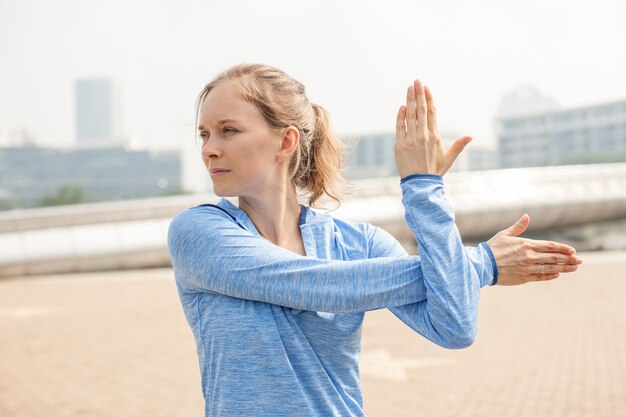 Ernstige sportieve Girl Stretching Arm buitenshuis