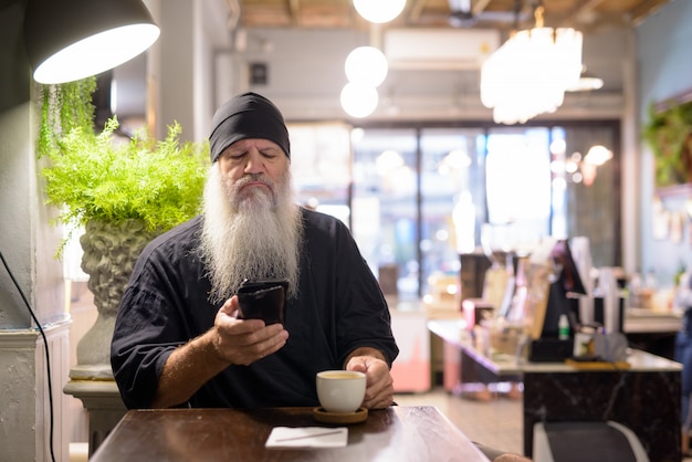 Ernstige volwassen bebaarde hipster man met behulp van telefoon in de coffeeshop