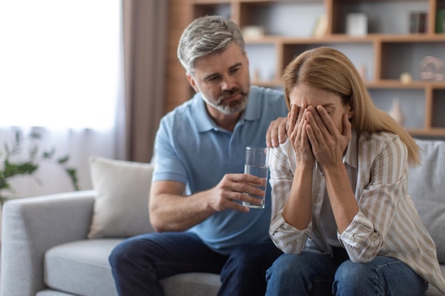 Ernstige volwassen blanke echtgenoot kalm overstuur huilende vrouw geeft glas water dame lijdt aan pijn en depressie