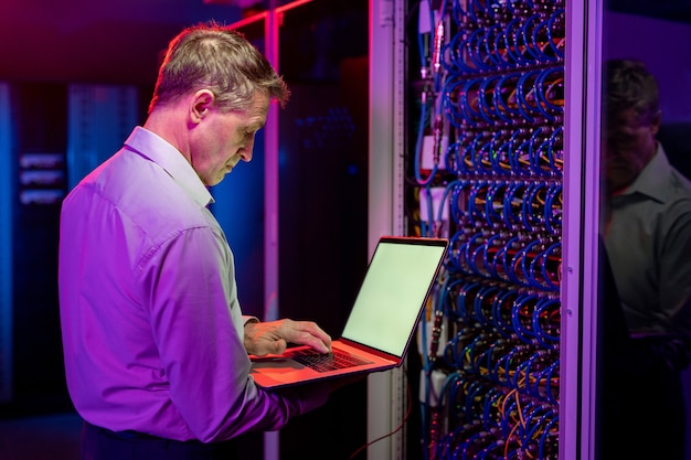 Ernstige volwassen netwerkingenieur die bij een open serverkast staat en een laptop gebruikt tijdens het diagnosticeren van serverproblemen