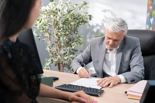 Ernstige werkgever oudere volwassen baas met grijs haar gekleed in pak zit in een fauteuil aan bureau in