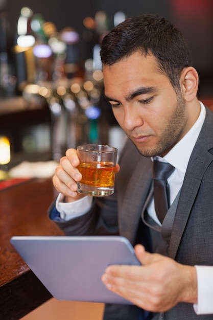 Ernstige zakenman die aan zijn tabletcomputer werkt terwijl het hebben van een whisky