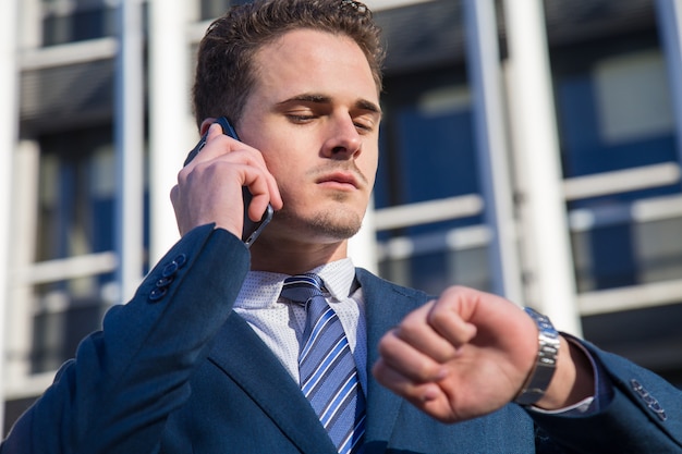 Ernstige zakenman die tijd controleert die op telefoon spreekt.