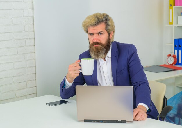 Ernstige zakenman met laptop en beker zakelijke deskundige zakenman die met laptop op kantoor werkt