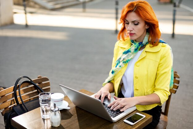 Ernstige zakenvrouw die op de laptop werkt aan een koffiepauze in een straatcafé.