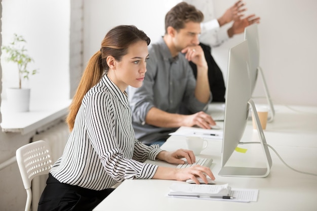 Ernstige zakenvrouw die op een personal computer werkt in een coworking-ruimte, e-mails schrijft aan zakelijke klanten, doordachte werker die op internet surft en financieel nieuws leest om bedrijfsstatistieken te controleren