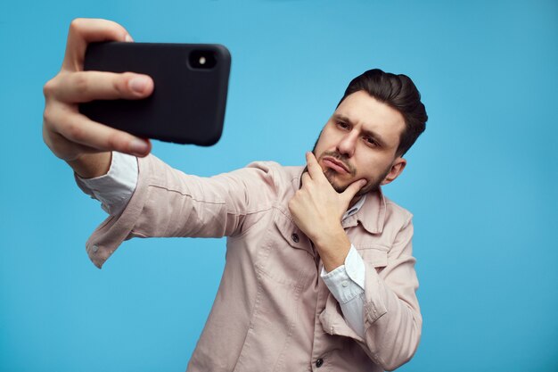 Ernstige zelfverzekerde bebaarde man die een selfie maakt met smartphone over blauw