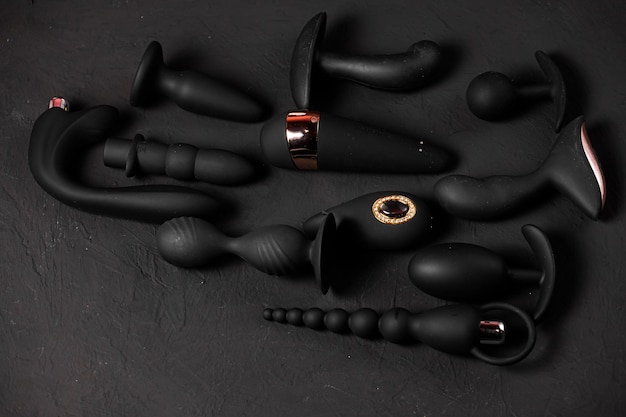 Erotic pleasure toys on a black background Sex gadgets and masturbation devices Pink dildo surrounded by black rubber and silicone sex toys anal butt plugs vibrators vaginal balls Top view