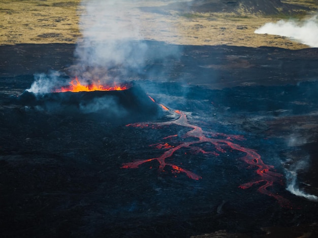 噴火する火山の赤い熱い沸騰する溶岩がクレーターから荒廃した周辺地域に流れ出しています