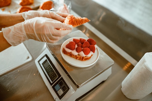 Ervaren banketbakker zet top op croissant met sappige aardbeien en room in ambachtelijke bakkerij