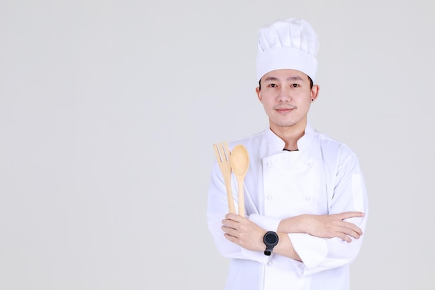 Ervaren en slimme chinese chef-kok met een elegante kookuniforme glimlach en zelfverzekerd in de keuken met gekruiste arm en lepel als gekwalificeerde keukenexpert voor luxueus dineren in het restaurant.