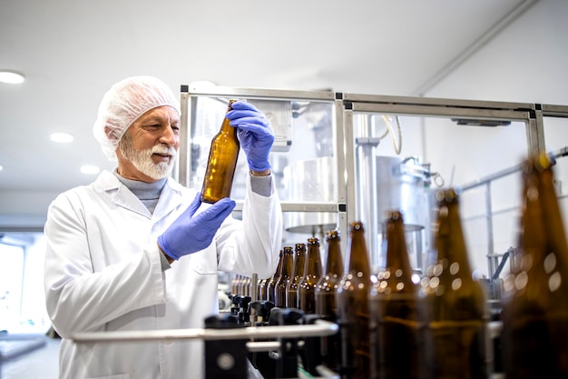 Ervaren fabrieksarbeider die de productie van bierflesjes in de drankenfabriek controleert