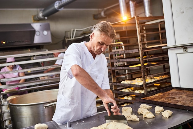 Ervaren man bakker die rauw deeg in gelijke porties verdeelt en ze weegt Proces van het maken van brood in de bakkerij