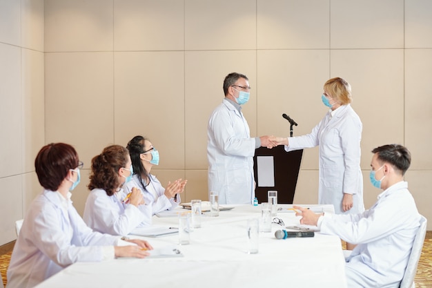 Ervaren onderzoekers met medische maskers die handen schudden na een succesvolle medische conferentie gewijd aan coronavirus