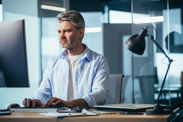 Ervaren werknemer grijsharige zakenman werkt op de computer in een modern kantoor