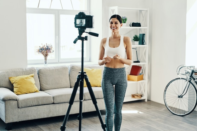 Ervaring delen. Mooie jonge vrouw in sportkleding die video op sociale media maakt terwijl ze thuis tijd doorbrengt