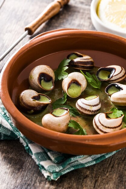 Escargots de Bourgogne with green sauce in bowl on wooden table