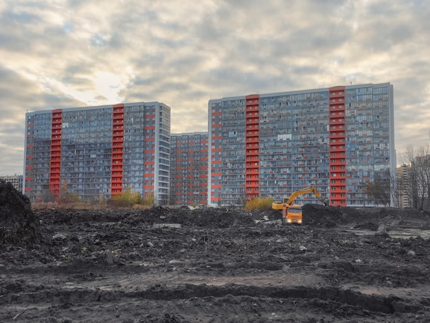 エスカベーターは、夕方に新しい家を建設するために土をトラックに積み込みます 近代的な地区に新しい住宅を建設する