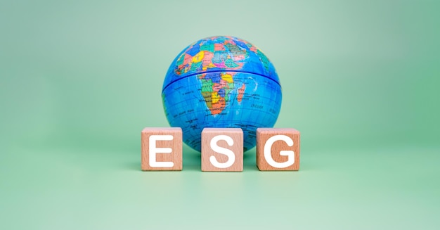 Фото Концепция esg для окружающей среды общества и управления в устойчивом бизнесе ответственные экологические деревянные блоки с напечатанными на них буквами esg и моделью земли на зеленом фоне