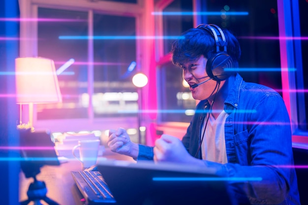 Esport online game streaming asian male wear headset play dogital metaverse cyber space online match compettition sport game battle night timeyoung asia male enjoy exited gamer successful celebration