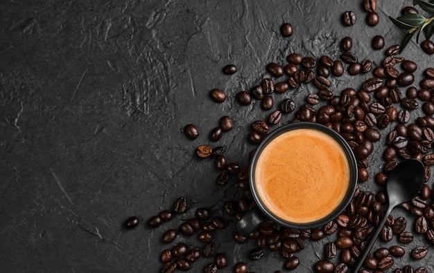 Espresso coffee with fragrant foam in a cup on a black background, flat lay. Breakfast with Italian cafe, top view of a cup of coffee, coffee grains are scattered on the table. copy space for text