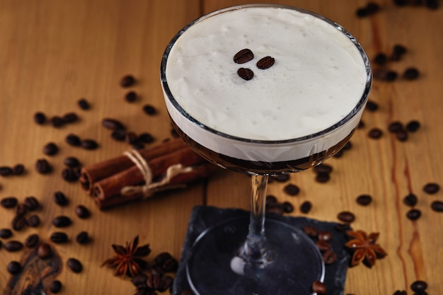 Espresso martini cocktail in een glas met koffiebonen, kaneel en steranijs op een houttafel