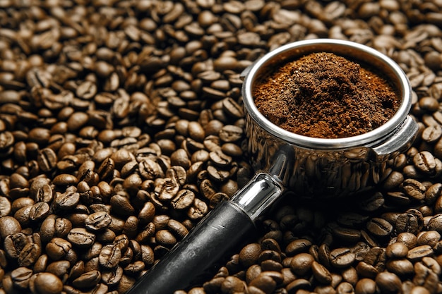 Espresso Portafilter Filled With Freshly Ground Coffee Beans Resting On Bed Of Roasted Coffee Beans