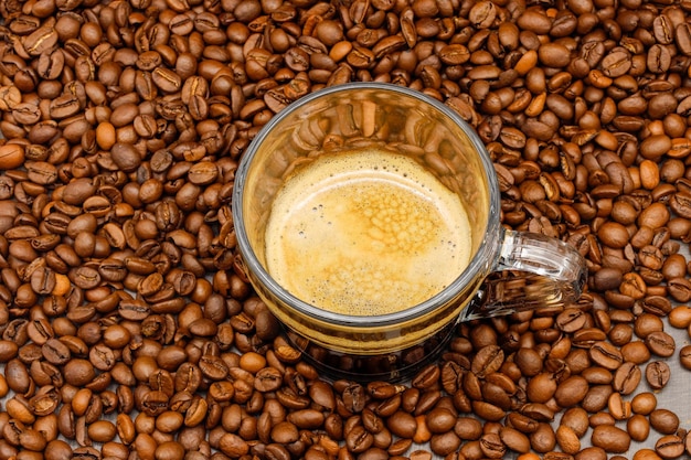 Espressokoffie in glazen beker met koffiebonen op houten tafel.