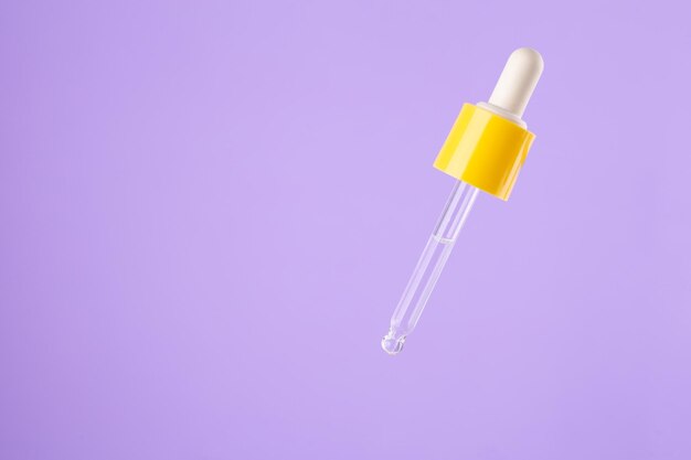 Essential clear oil or serum in pipette isolated on purple background close up cosmetic pipette