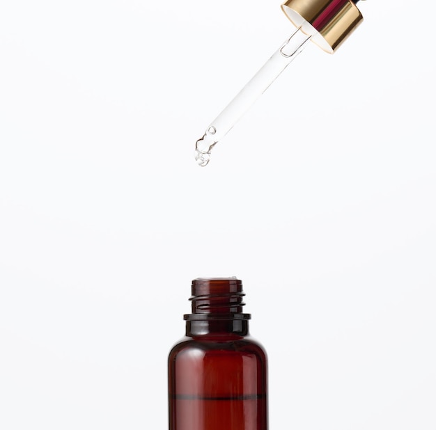 Photo essential oil falling from the amber glass dropper. blue bottle of cosmetic oil with a pipette, white background