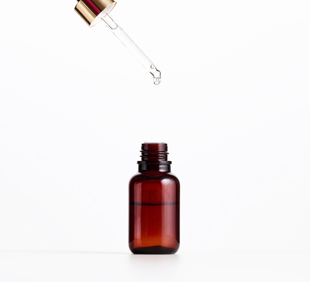 Photo essential oil falling from the amber glass dropper. blue bottle of cosmetic oil with a pipette, white background