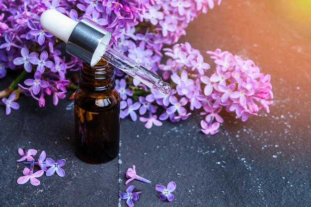 Essential oil of lilac flowers on a dark marble background illuminated by a sunbeam