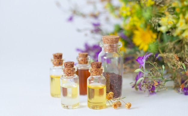 Essential oils in glass bottles with organic healing herbs and flowers in the light background