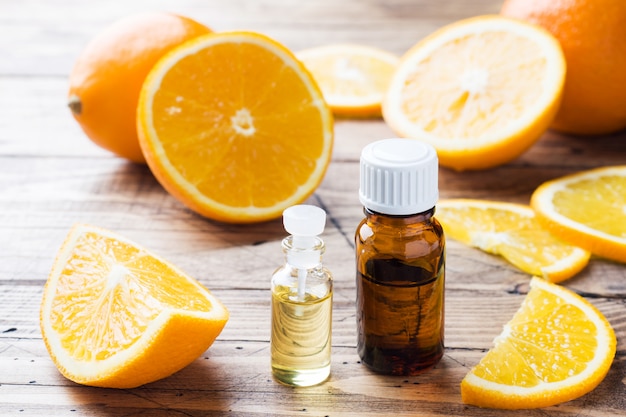 Essential orange oil in bottle, fresh fruit slices on wooden background. Natural fragrances.