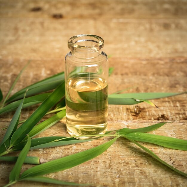 Foto essentiële olie in een kleine glazen fles met groene bamboeblaadjes op een houten achtergrond
