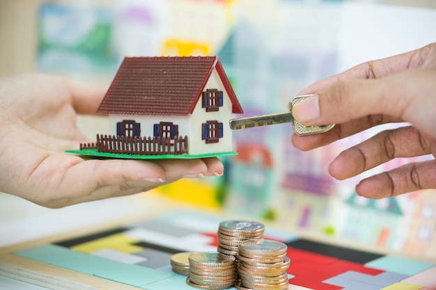 Photo estate agent and customer exchanging house model and key in hands.