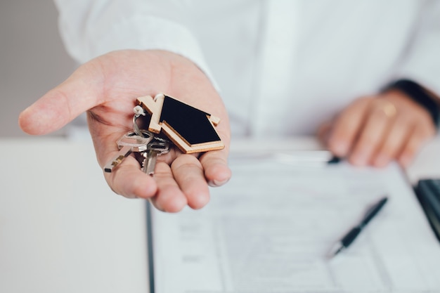 Agente immobiliare mano che tiene le chiavi di casa con portachiavi a forma di casa. concetto di ipoteca. immobile, trasloco o affitto di proprietà.