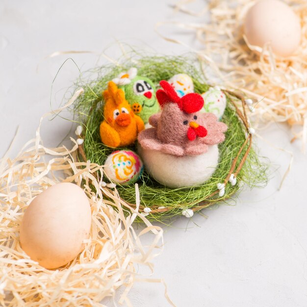 Ester chicken bunnys and eggs on straw against the background of decorative colored eggs made of wool