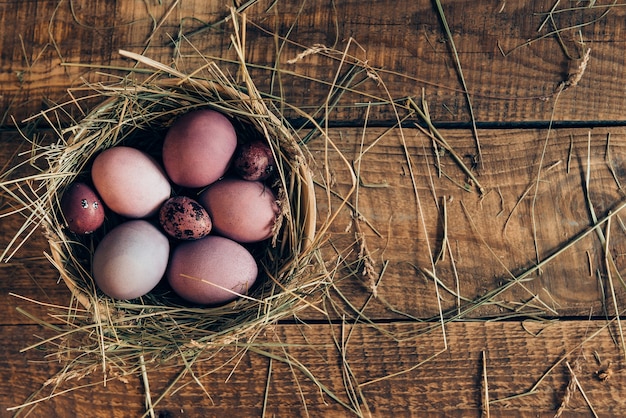 Ester nest. Top view of colored Easter eggs in bowl with hay lying on wooden rustic table