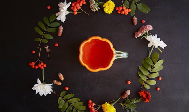 Esthetische herfst duurzame ecovriendelijke theetijd met creatieve beker in de vorm van pompoen natuurlijke achtergrond onder lijsterbessen eikels goudsbloem chrysant op zwarte achtergrond